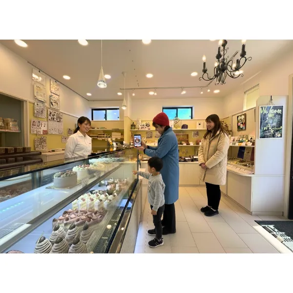 パティスリー・レ・トロワ・ソレイユの店内で、スマートフォンを手にケーキを選ぶお客様